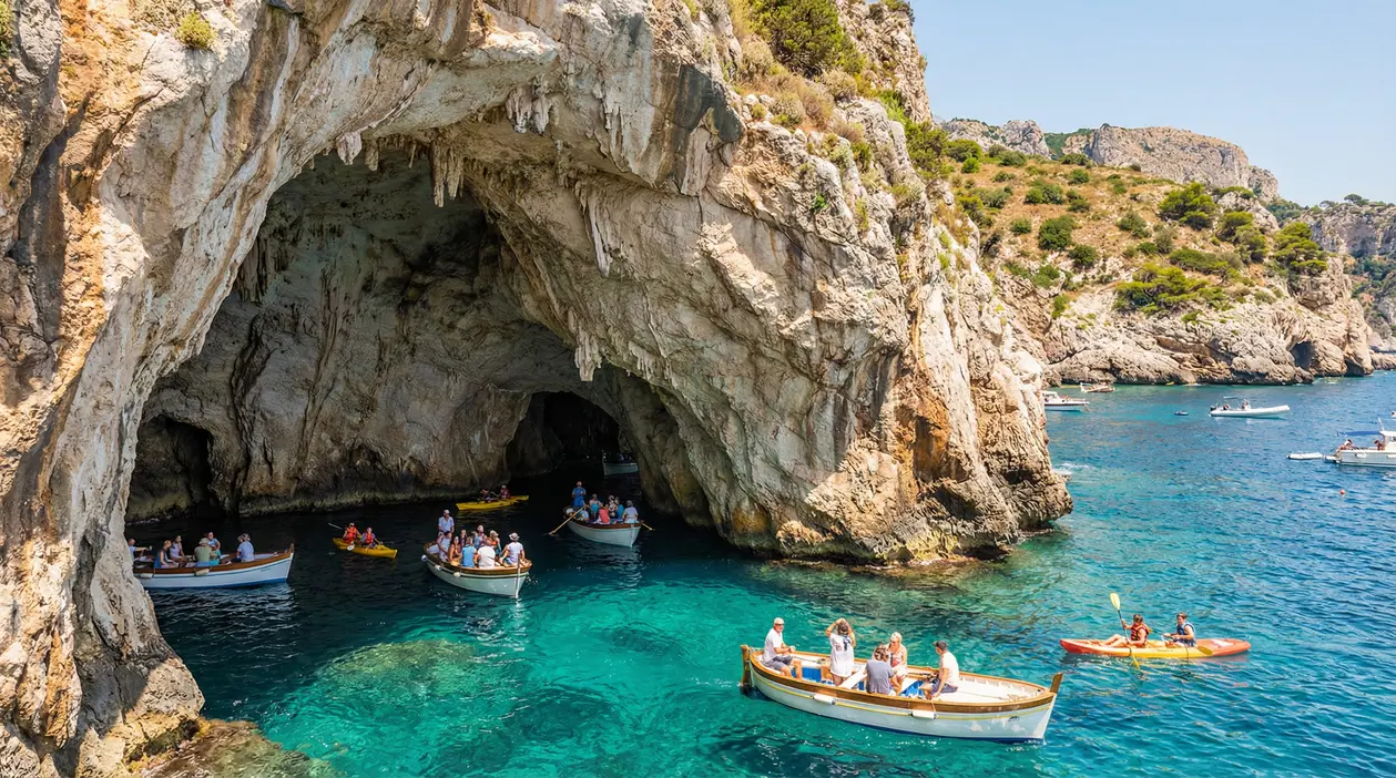 Grande grotta marina in una scogliera, con barche e kayak su acqua turchese durante una visita