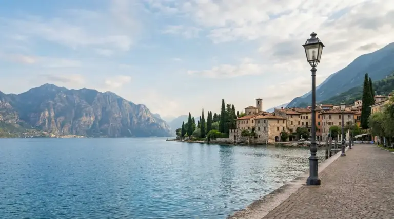 Lungolago tranquillo sul Lago di Garda con borgo storico, lampione e montagne sullo sfondo
