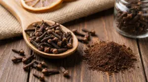 Chiodi di garofano interi in un cucchiaio di legno e polvere di chiodi su tavolo rustico